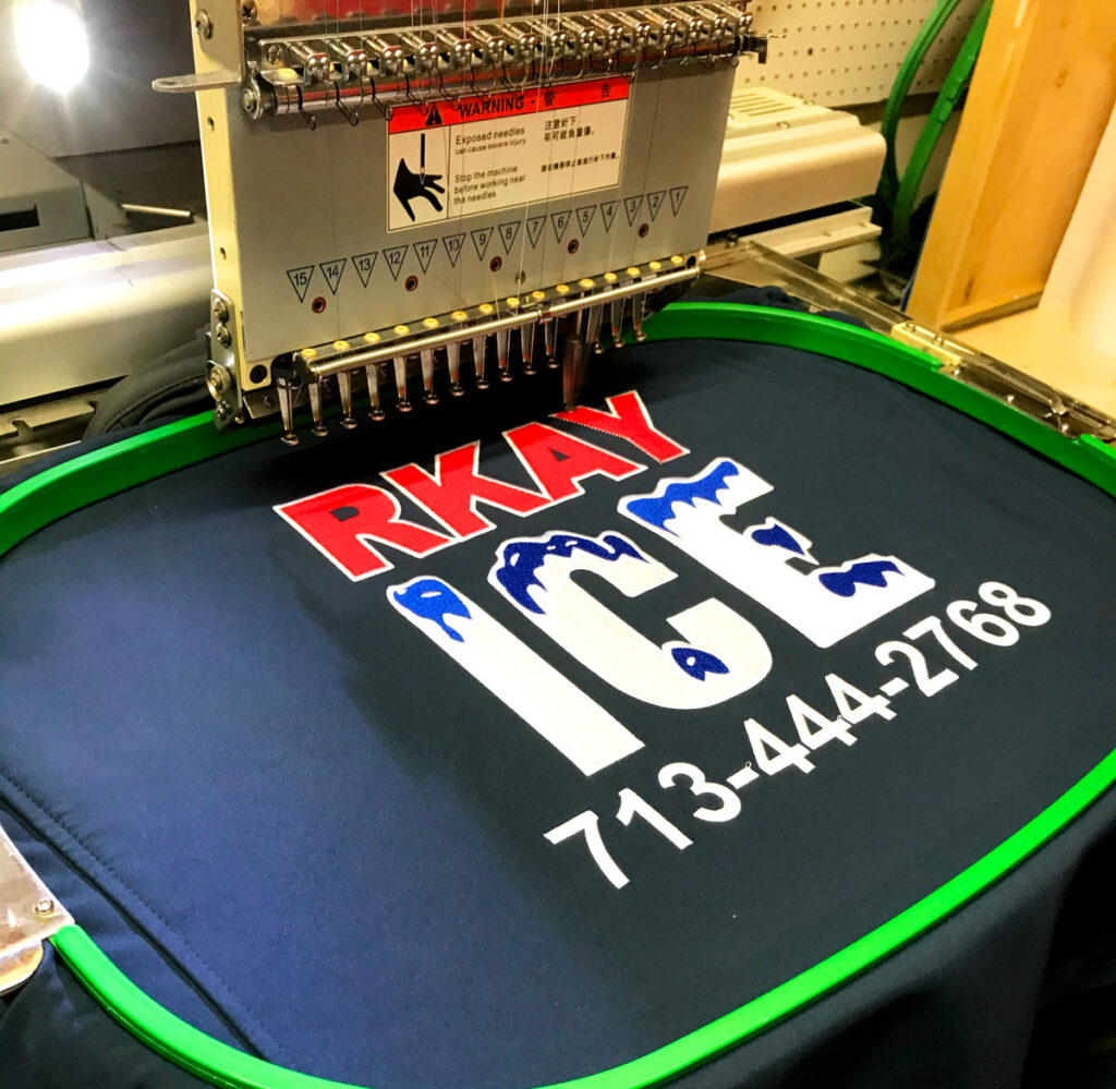 Commercial embroidery machine stitching a custom RKAY Ice logo on apparel at Ugly Guppy Productions, providing custom embroidery services in Houston, Texas.
