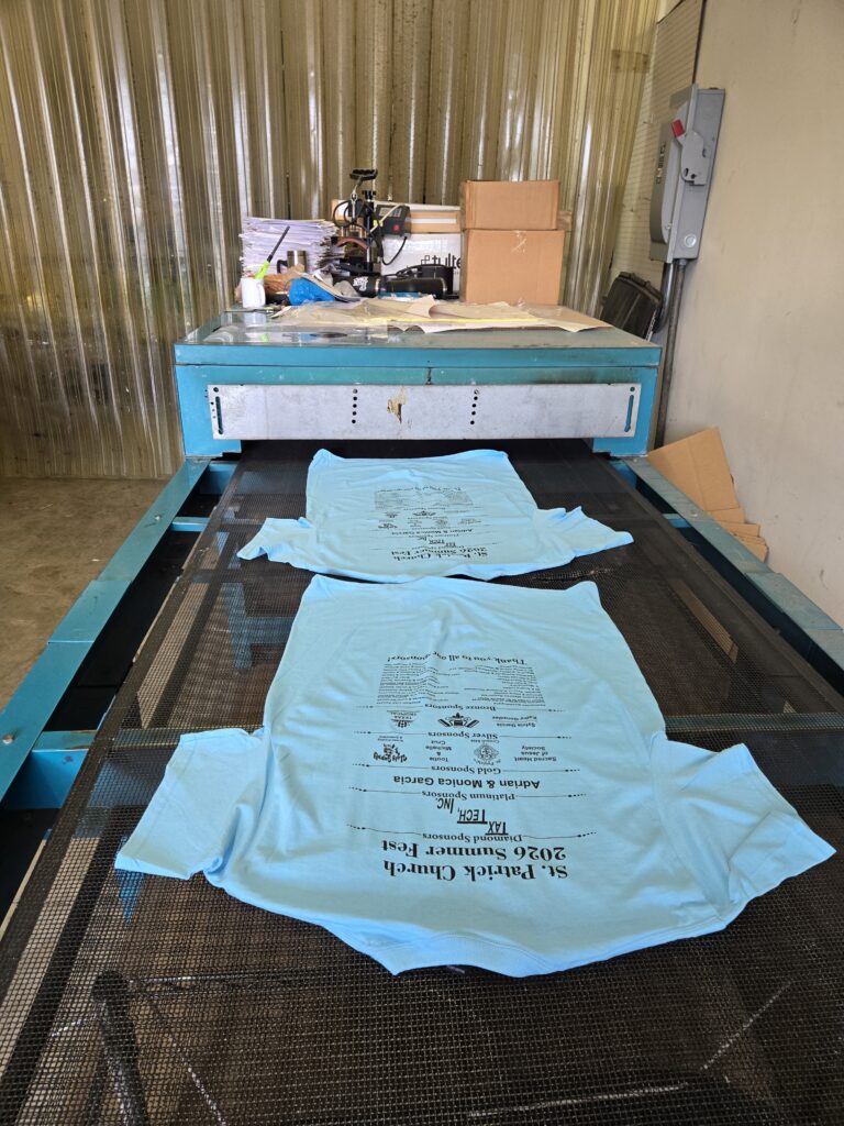 Screen-printed shirts moving through the production conveyor dryer at Ugly Guppy in Houston